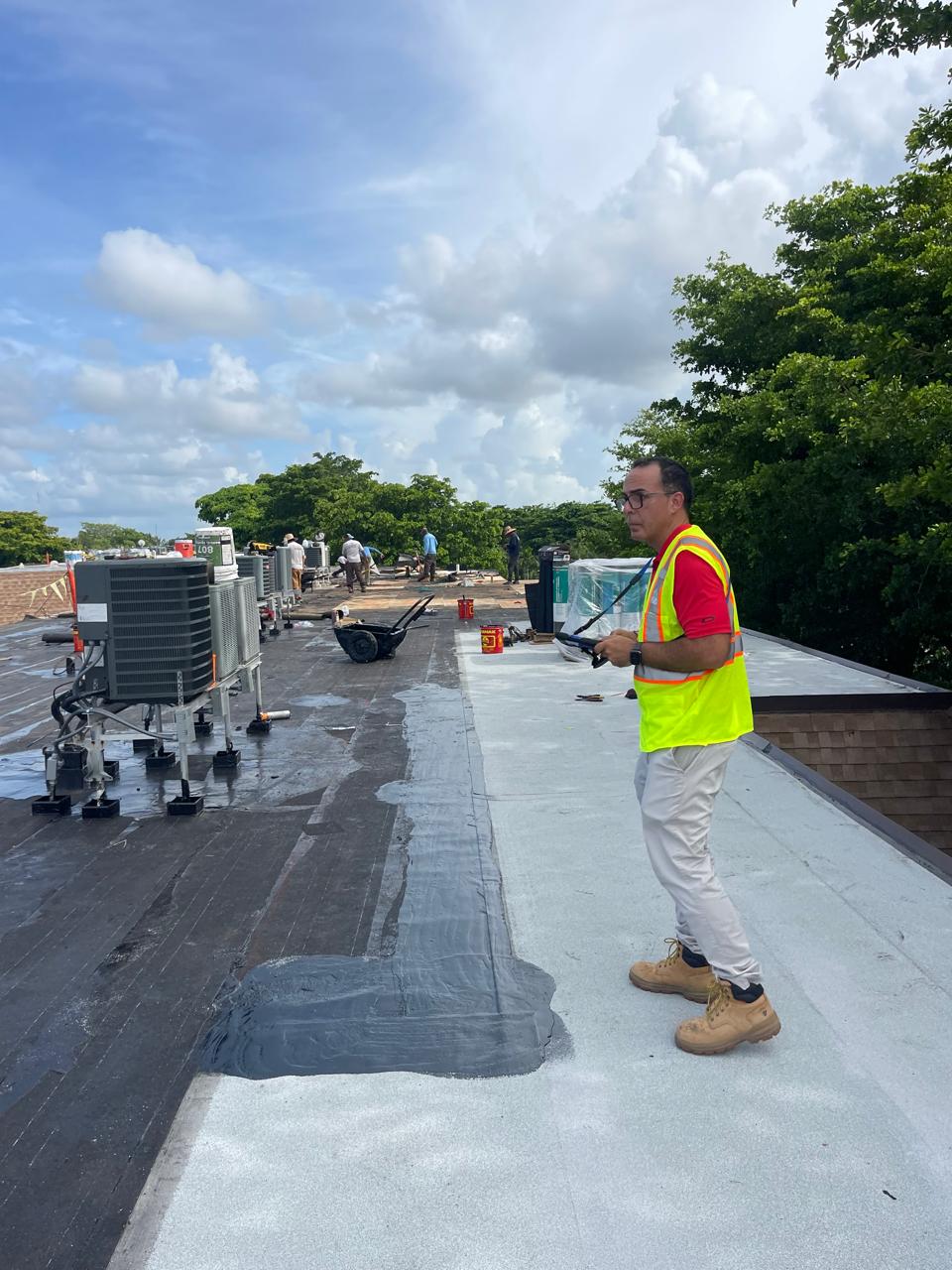 Man in red shirt using a drill on a window frame indoors.